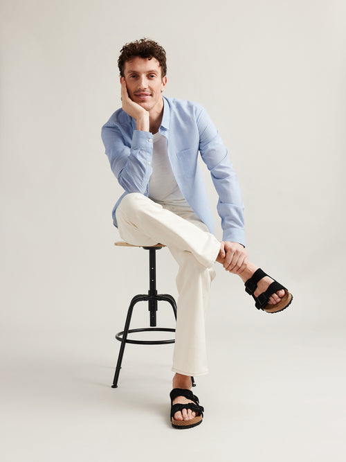 Man wears light blue chambray merino wool linen shirt in regular fit on white merino T-shirt and white trousers 