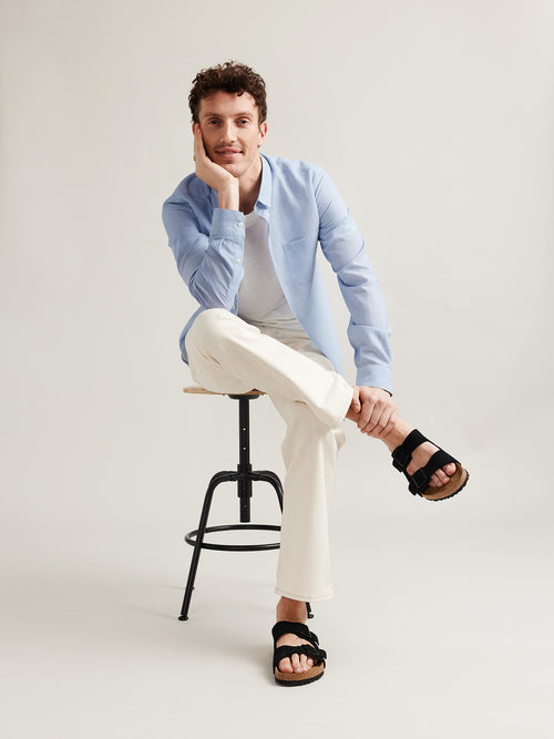 Man wears light blue chambray merino wool linen shirt in regular fit on white merino T-shirt and white trousers