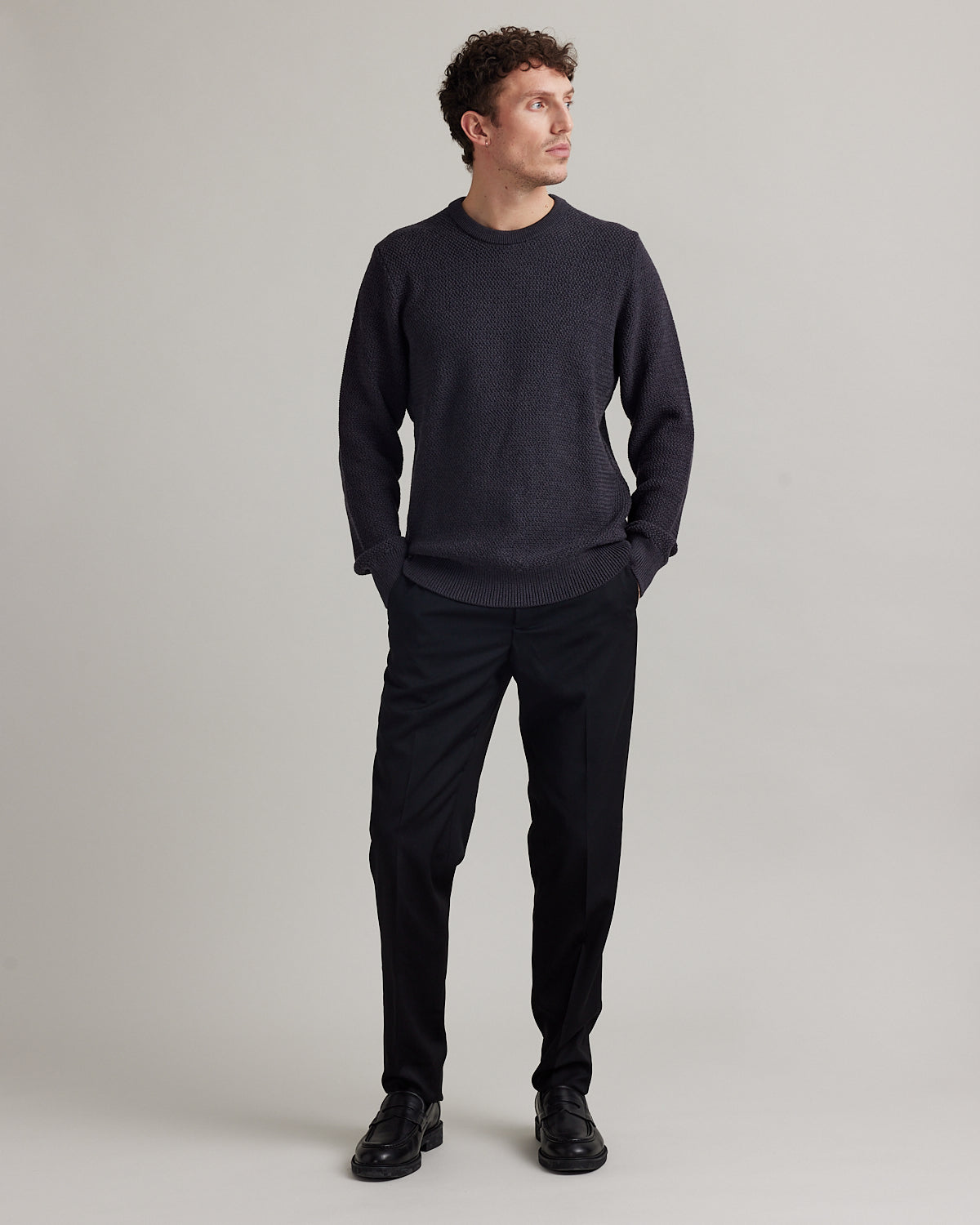 Man wears a dark grey merino wool sweater in rice knit with round collar and heavy weight warm jumper