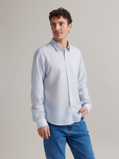 man wears a merino wool linen shirt with long sleeves and chest pocket in light blue bengal stripe on a jeans