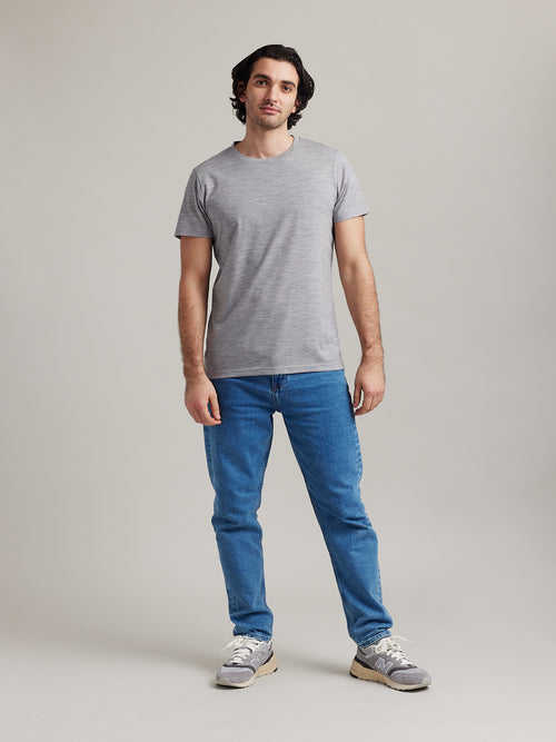 A male model in the studio wears a light grey merino wool T-shirt from the European Merino wool brand Wolk.