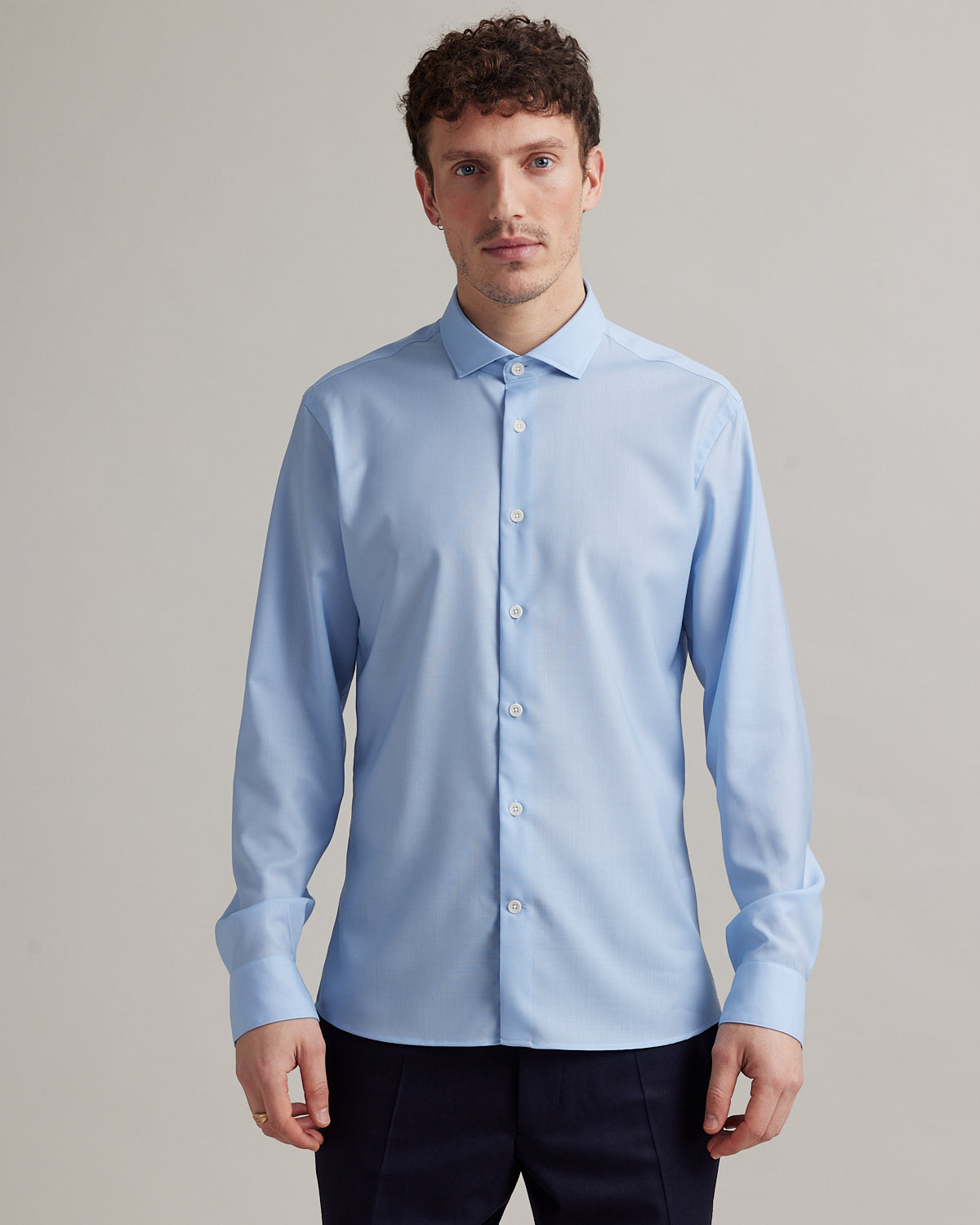 Man wears a light blue merino wool shirt with spread collar and white buttons in slim fit from Wolk