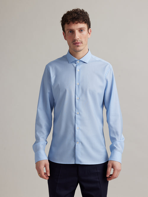 Man wears a light blue merino wool shirt with spread collar and white buttons in slim fit from Wolk