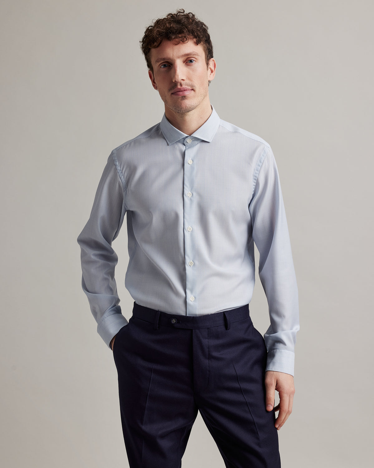 Man wears a light blue pinstripe merino wool formal shirt from Wolk with spread collar white buttons and long sleeves made in 100% merino wool