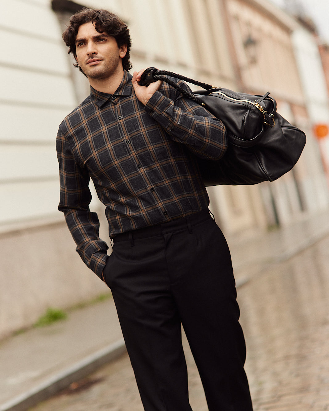Man wears a merino wool flannel shirt from Wolk in grey brown plaid pattern on a black trousers