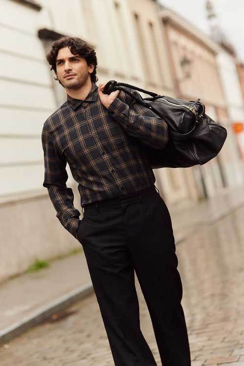 Man wears a merino wool flannel shirt from Wolk in grey brown plaid pattern on a black trousers