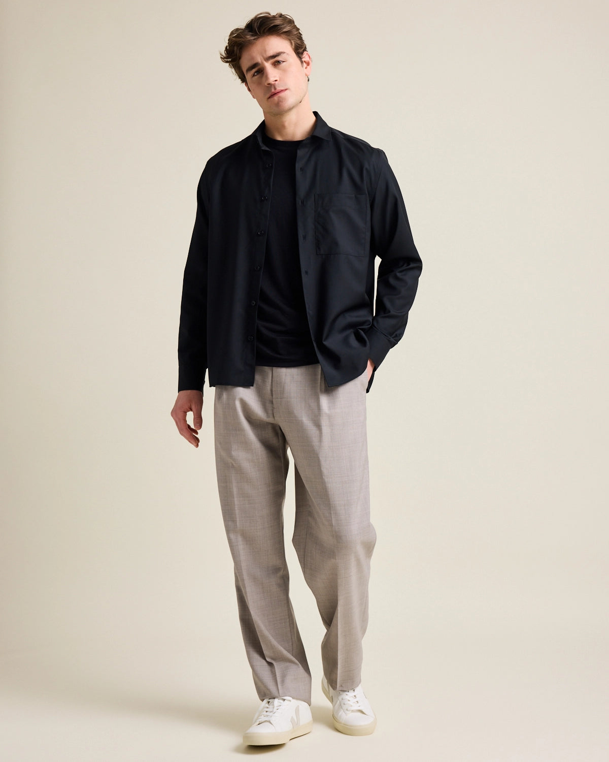 Man shows merino wool shirt from Wolk in black color on taupe wide fitted trousers.
