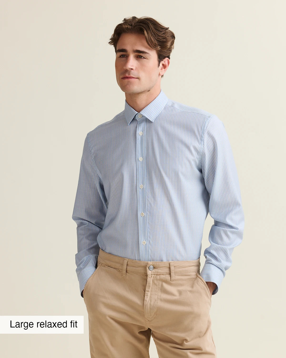 Man wearing a light blue striped merino shirt tucked in a beige pants on a beige background