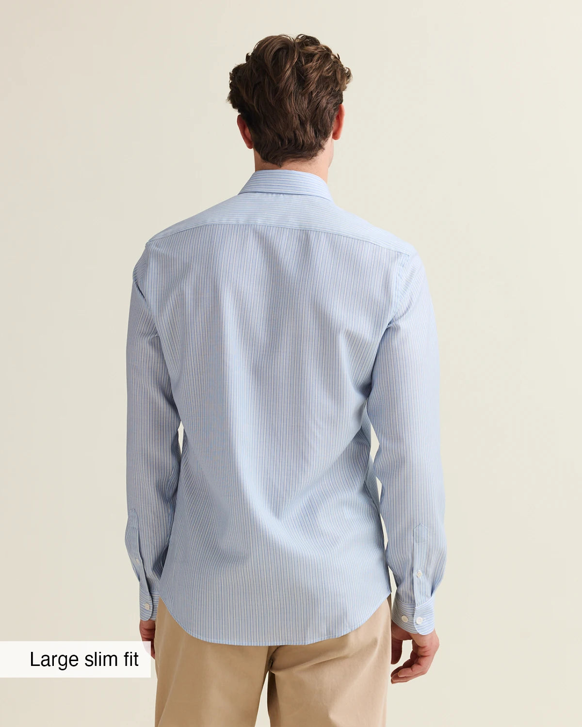 Back view of a Man wearing a light blue striped merino shirt and beige pants on a plain background