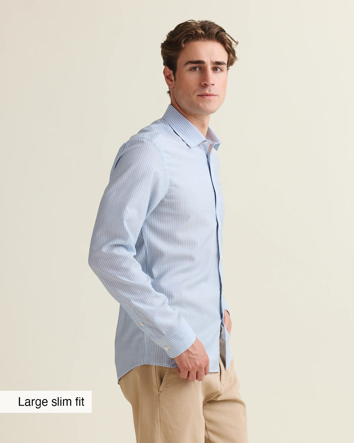 Side view of a Man wearing a light blue white striped merino shirt with beige pants on a beige background