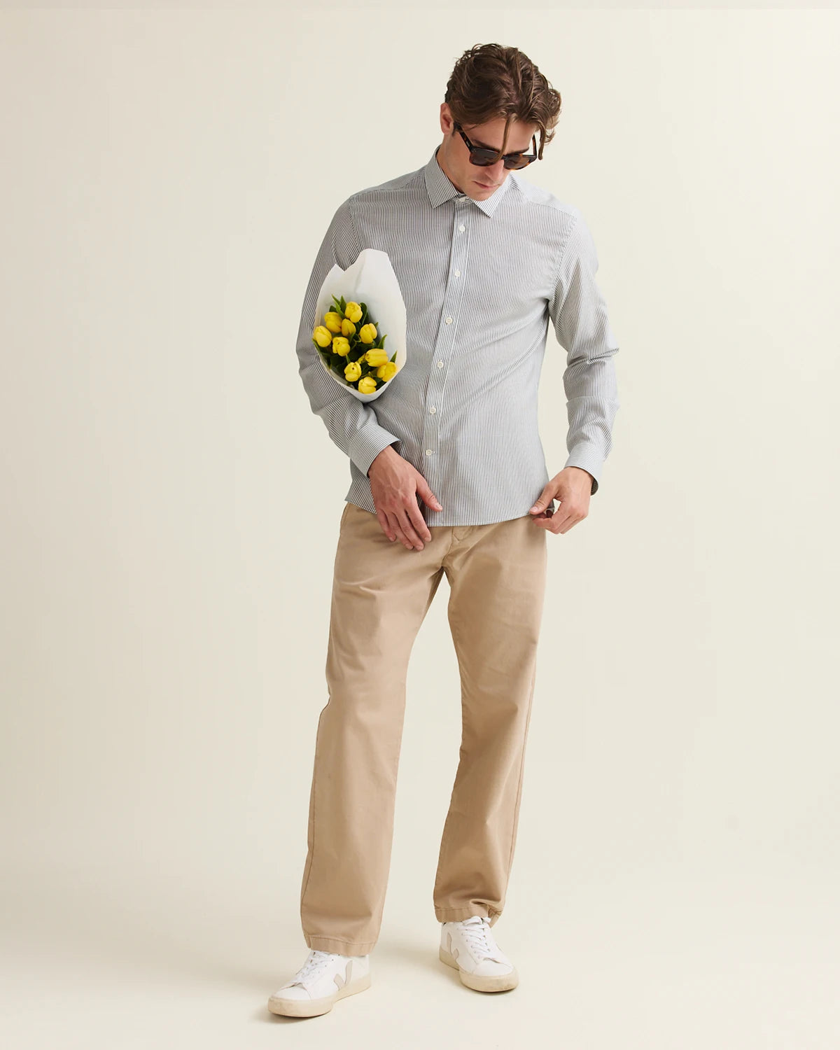 Man holding a bouquet of yellow flowers against a plain background