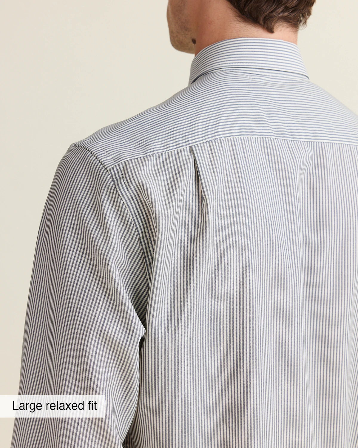 Close-up of of the back shoulder of a person wearing a navy bengal striped shirt against a beige background