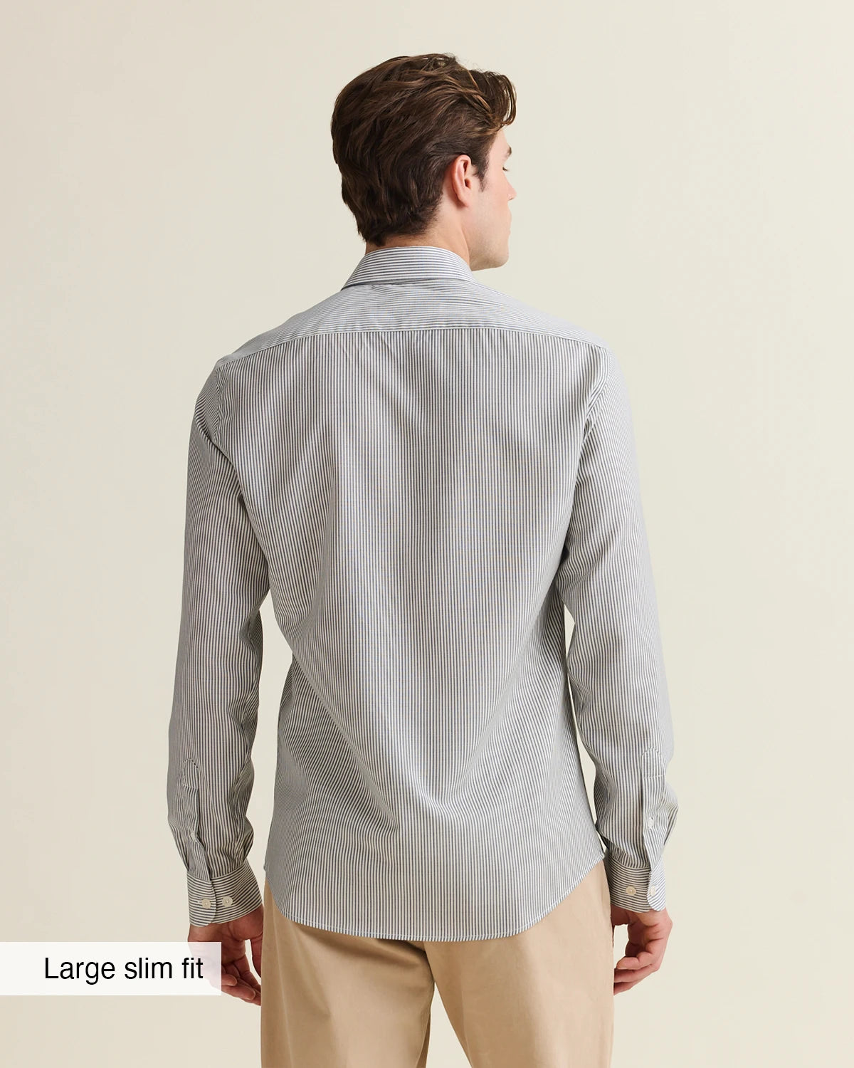 Backside of a man wearing a navy bengal striped merino shirt with a large slim fit label on a beige background