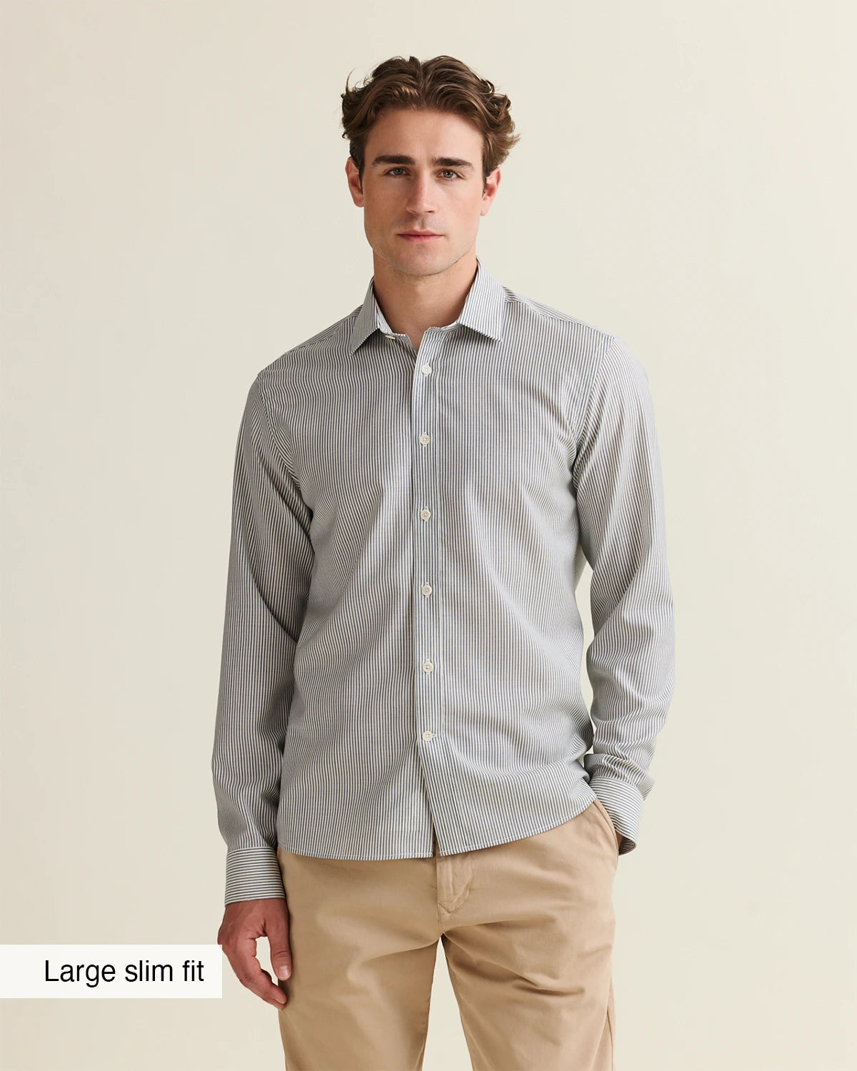 Front view of a man wearing a navy bengal striped merino wool shirt and beige pants on a beige background