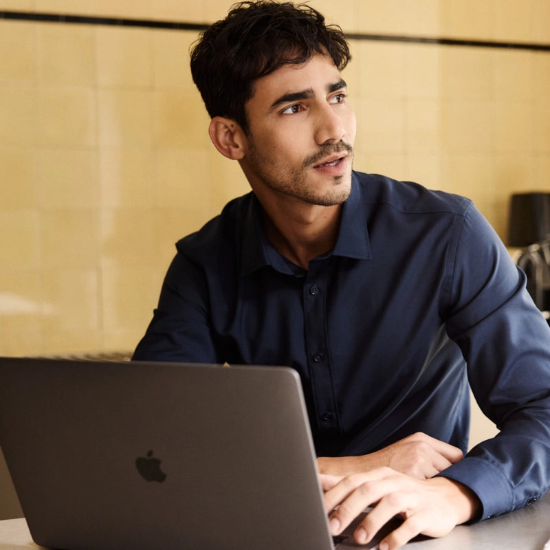 Man wearing a navy blue merino shirt from Wolk and using a laptop in a kitchen setting