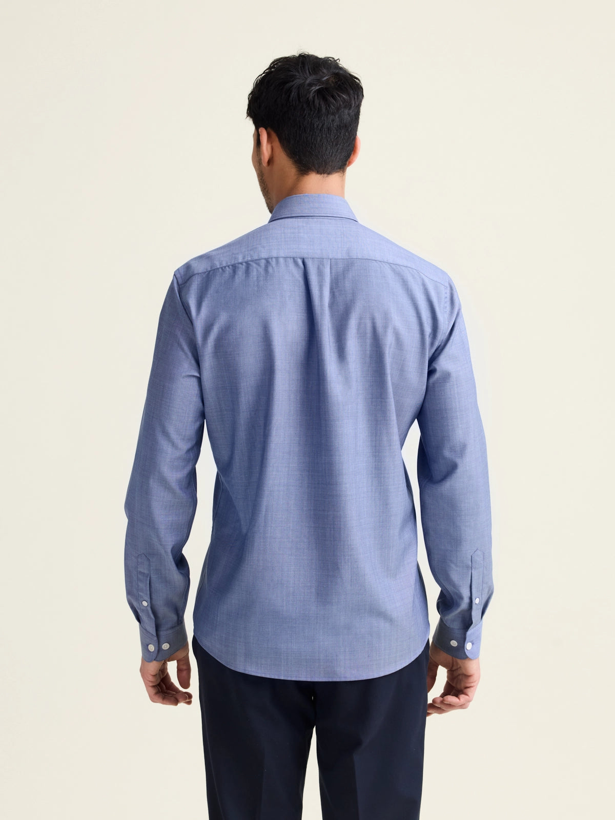 Backview of man wearing a light blue denim merino wool shirt with long sleeves untucked on a navy pants