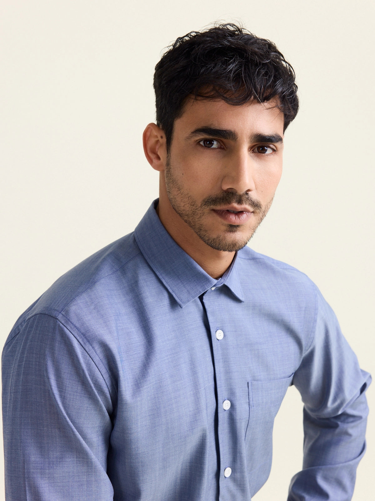 Man wears a merino wool shirt in light blue denim color with chest pocket and white buttons.