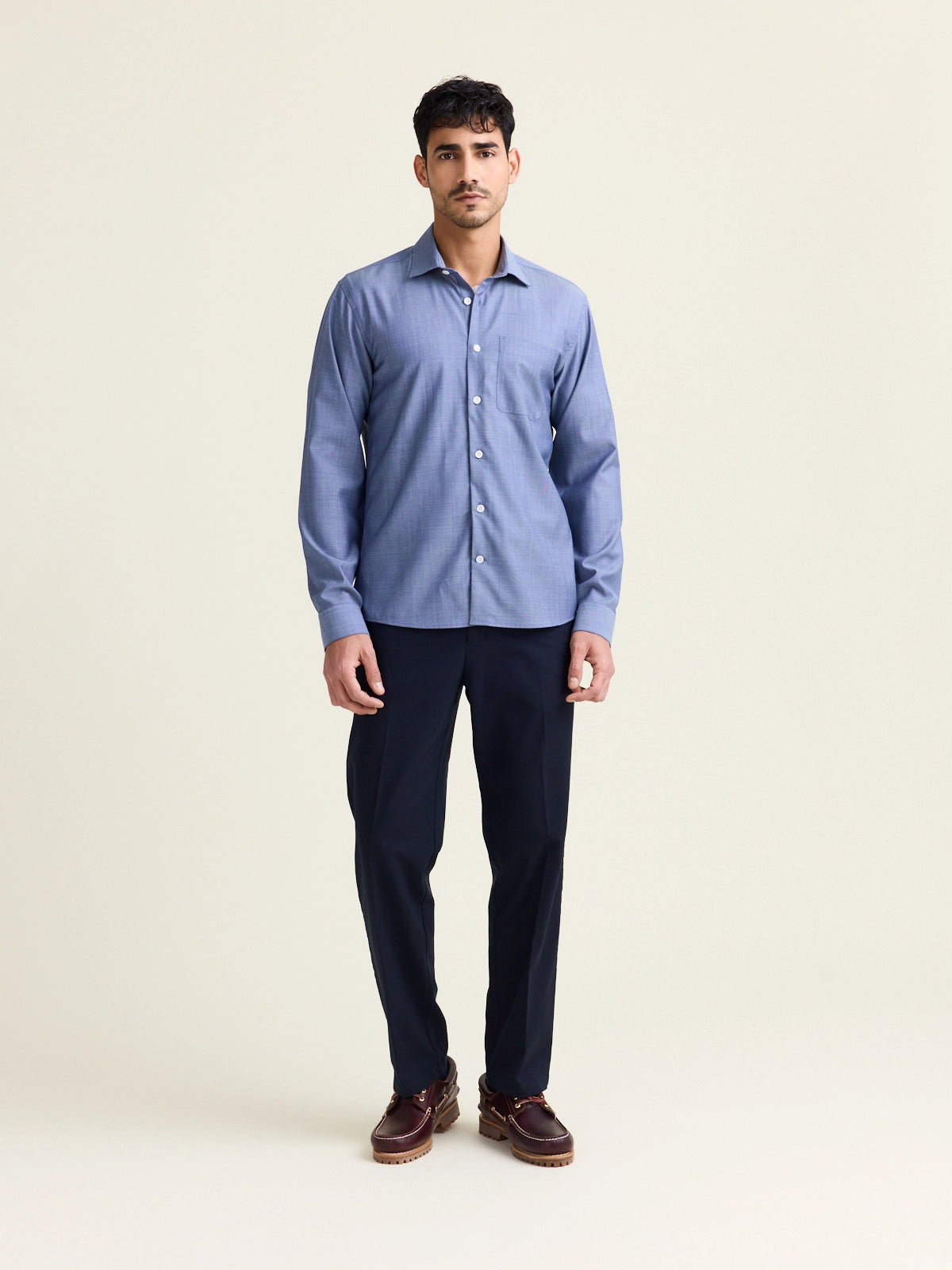 Full view of male model that wears a merino wool shirt in light blue denim color with chest pocket and white buttons.