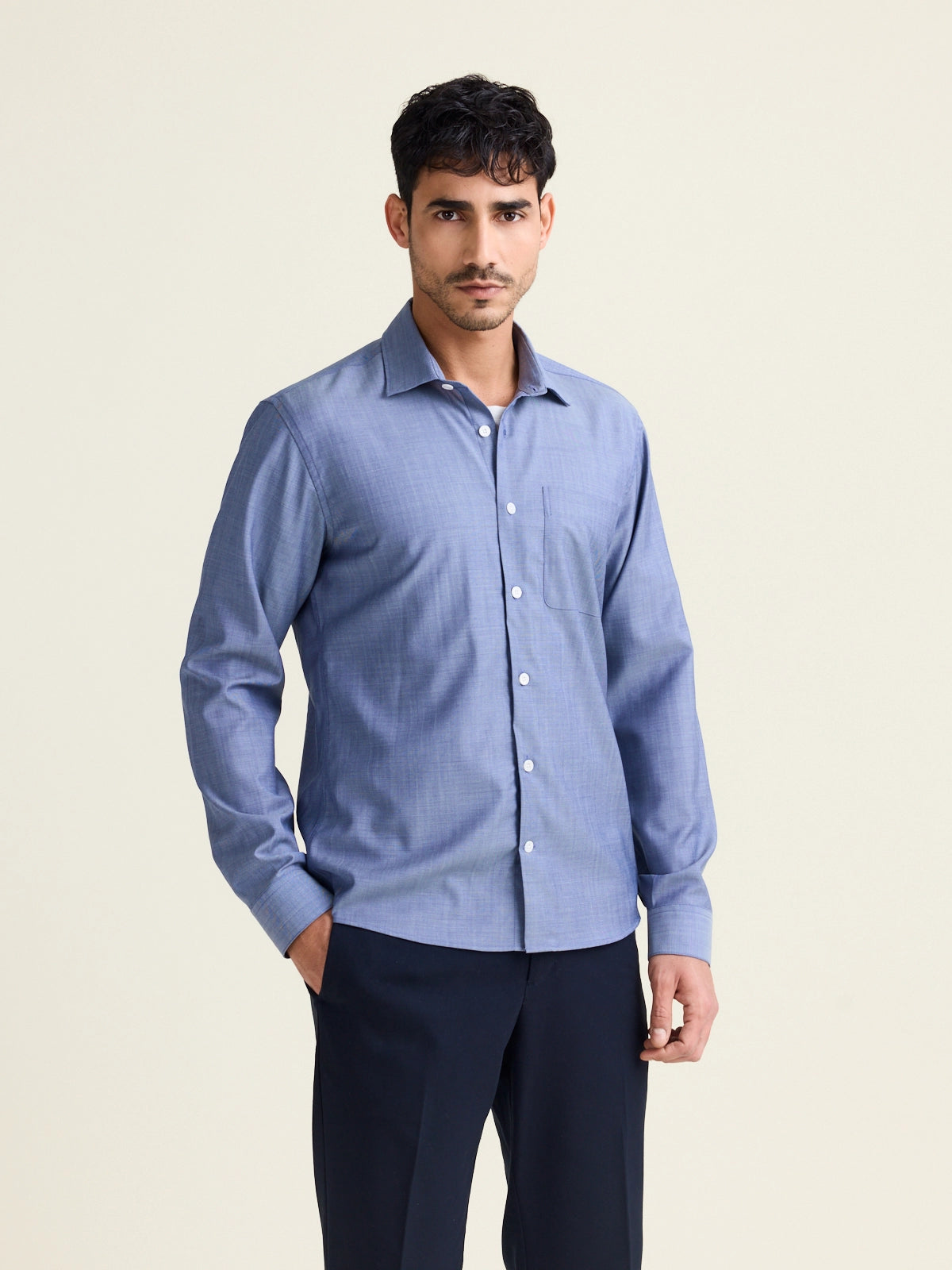 Man wears a merino wool shirt in light blue denim color with chest pocket and white buttons untucked on a navy pants