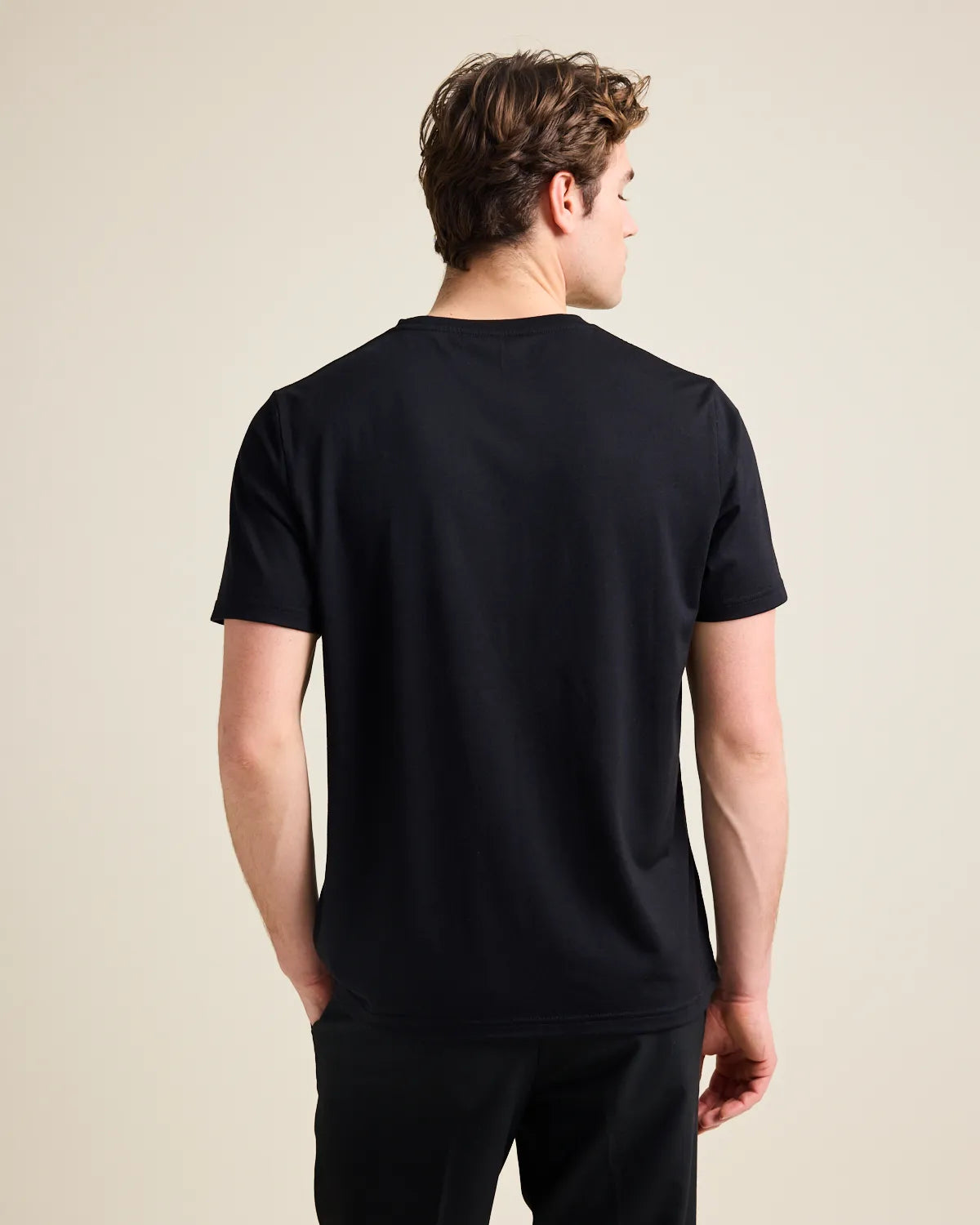 back view of a model wearing a black Tshirt on a beige background