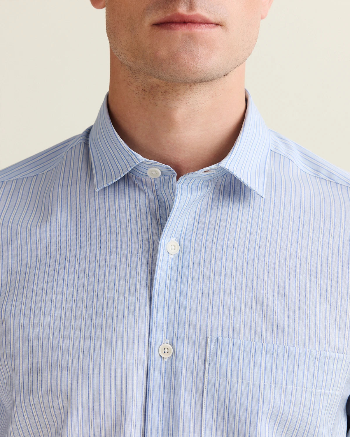 Close-up of the open collar of a person wearing a light blue striped merino wool shirt with a neutral background