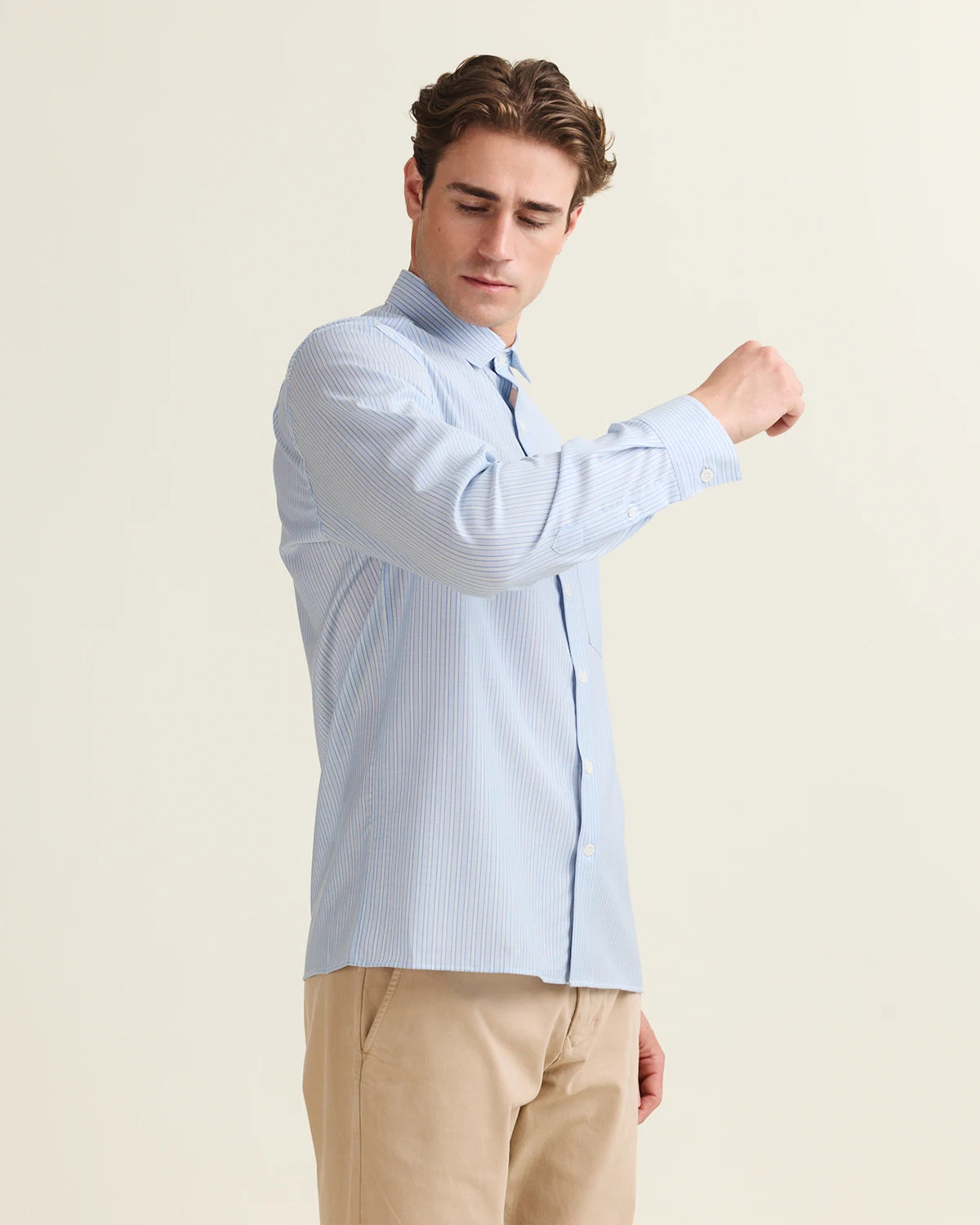 Man wearing a light blue white striped merino shirt and beige pants on a plain background