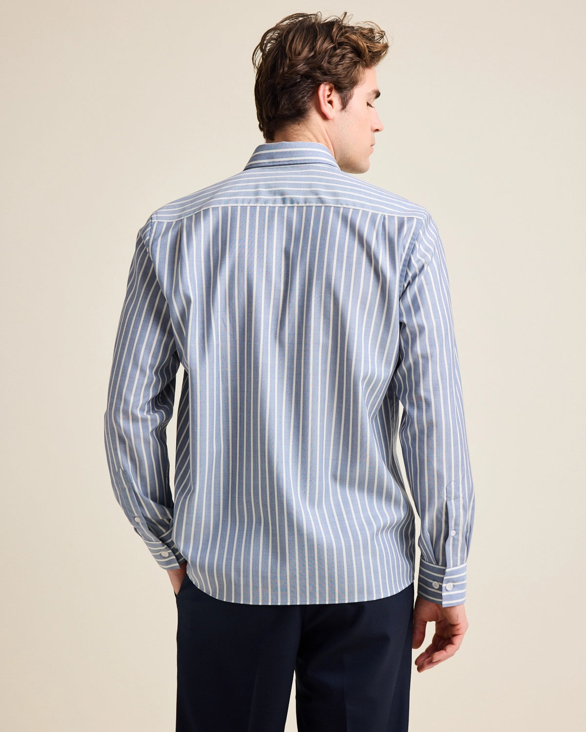 Back view of model wearing a blue with striped merino wool shirt on navy pants.