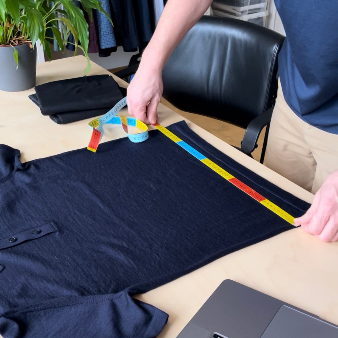 Person measuring a navy shirt on a table with a ruler Wolk merino wool garments are designed in Belgium
