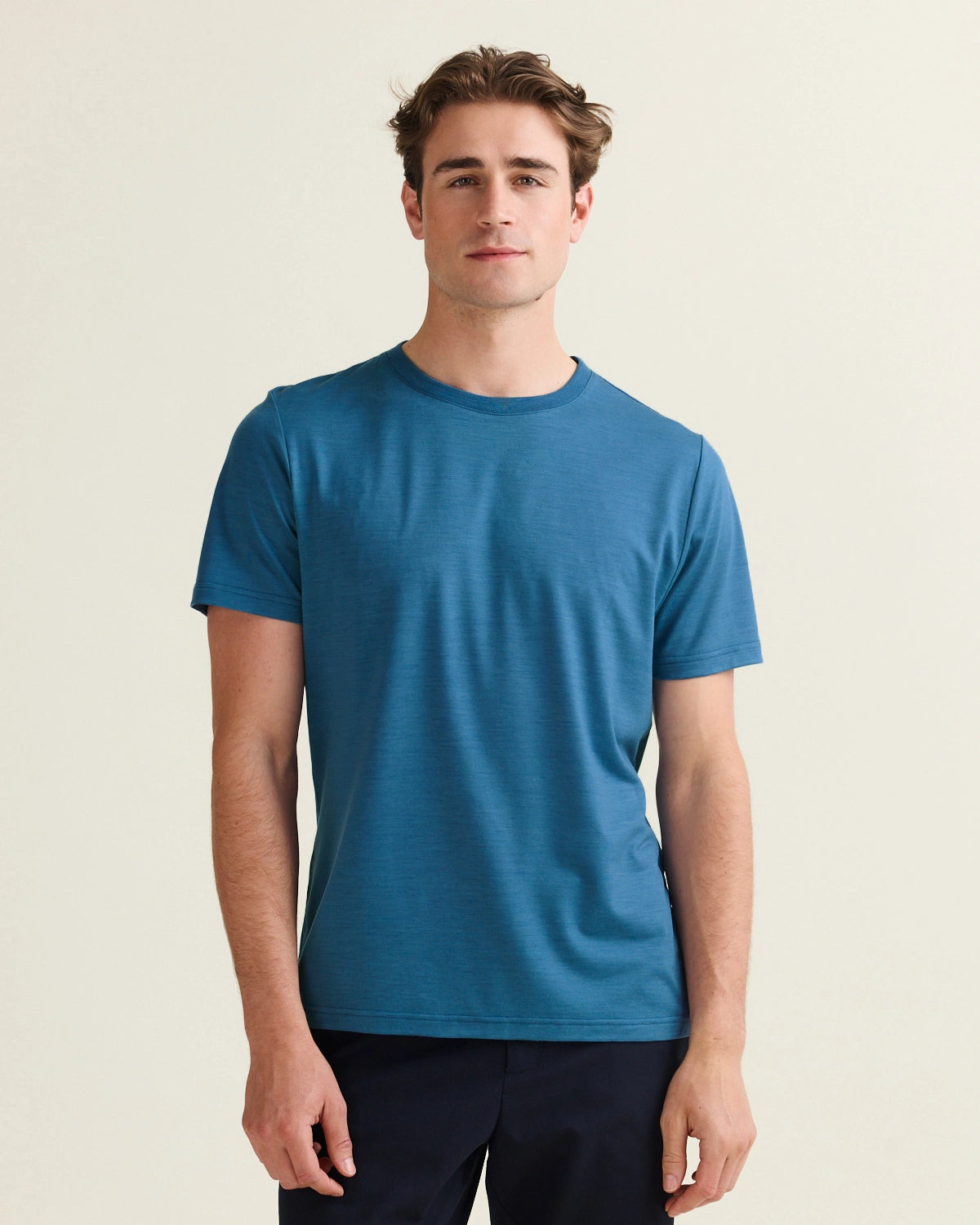 Man wearing a blue 17 micron merino wool t-shirt with short sleeves and crew neck against a beige background from Wolk brand