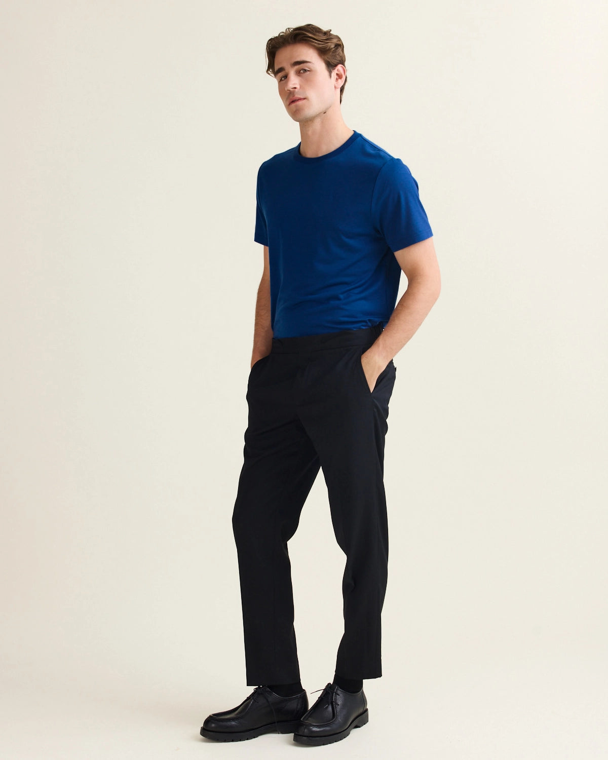 Man wearing a stylish blue merino wool t-shirt and black pants against a plain background
