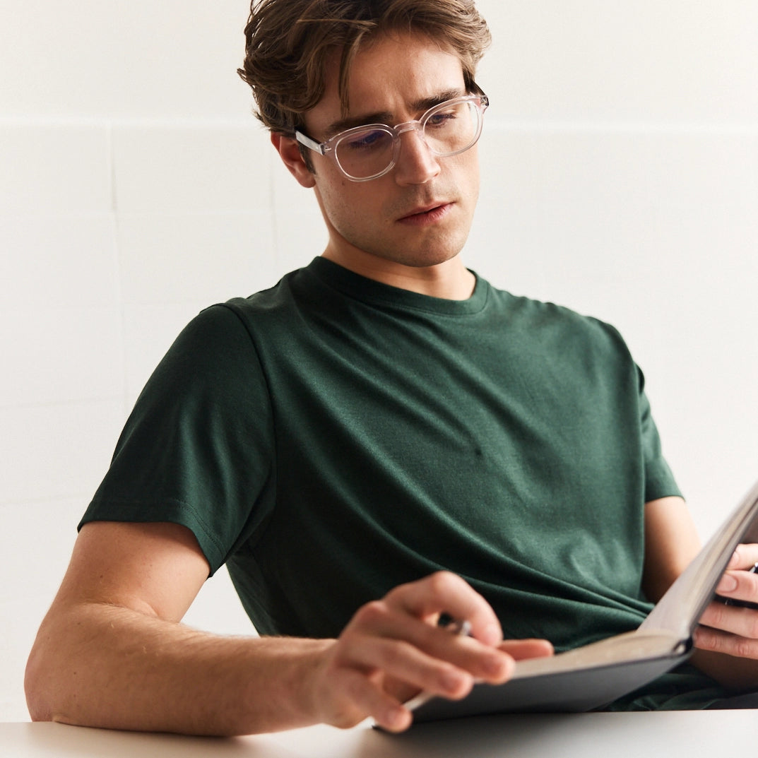 Man wearing a dark green merino wool T-shirt with short sleeves sitting in an office