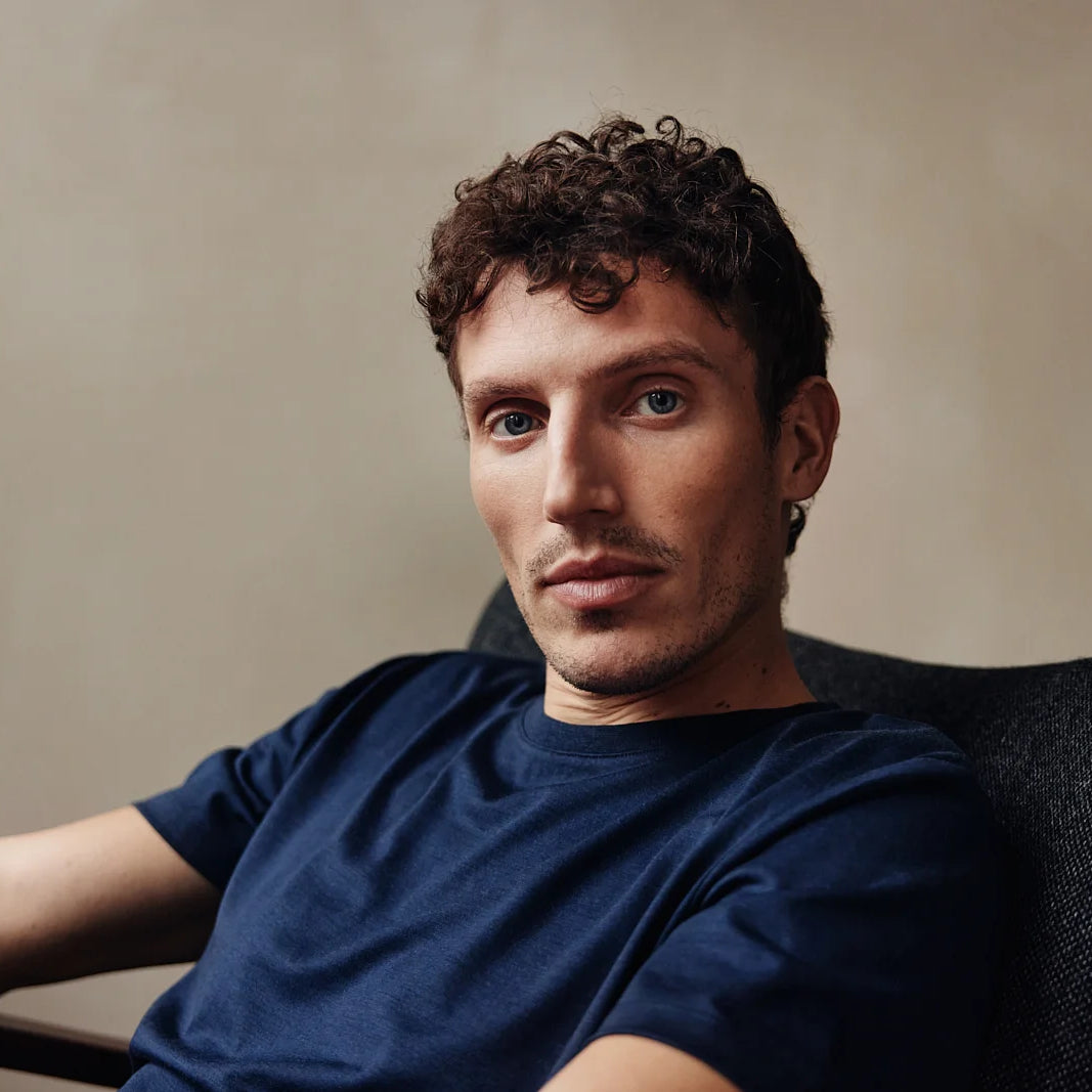 Man sits in chair and wears a navy merino wool T-shirt from Wolk