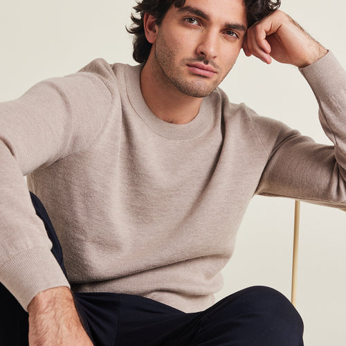 Man wears a 100% merino wool sweater in taupe color on a navy trousers round collar mid weight all year round pullover