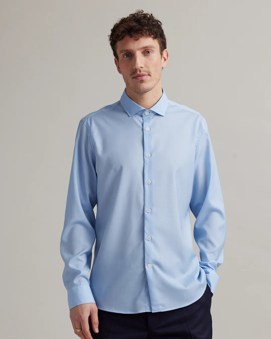 Man wearing a light blue dress shirt in merino wool with spread collar against a plain background
