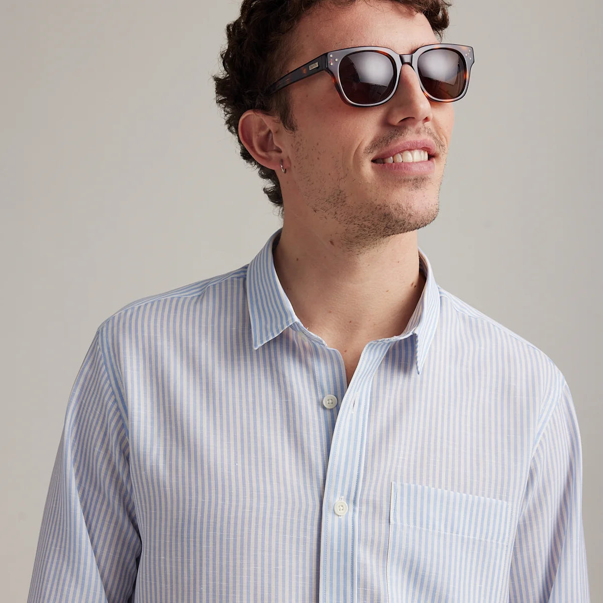 Man wearing a striped merino wool shirt and sunglasses against a plain background