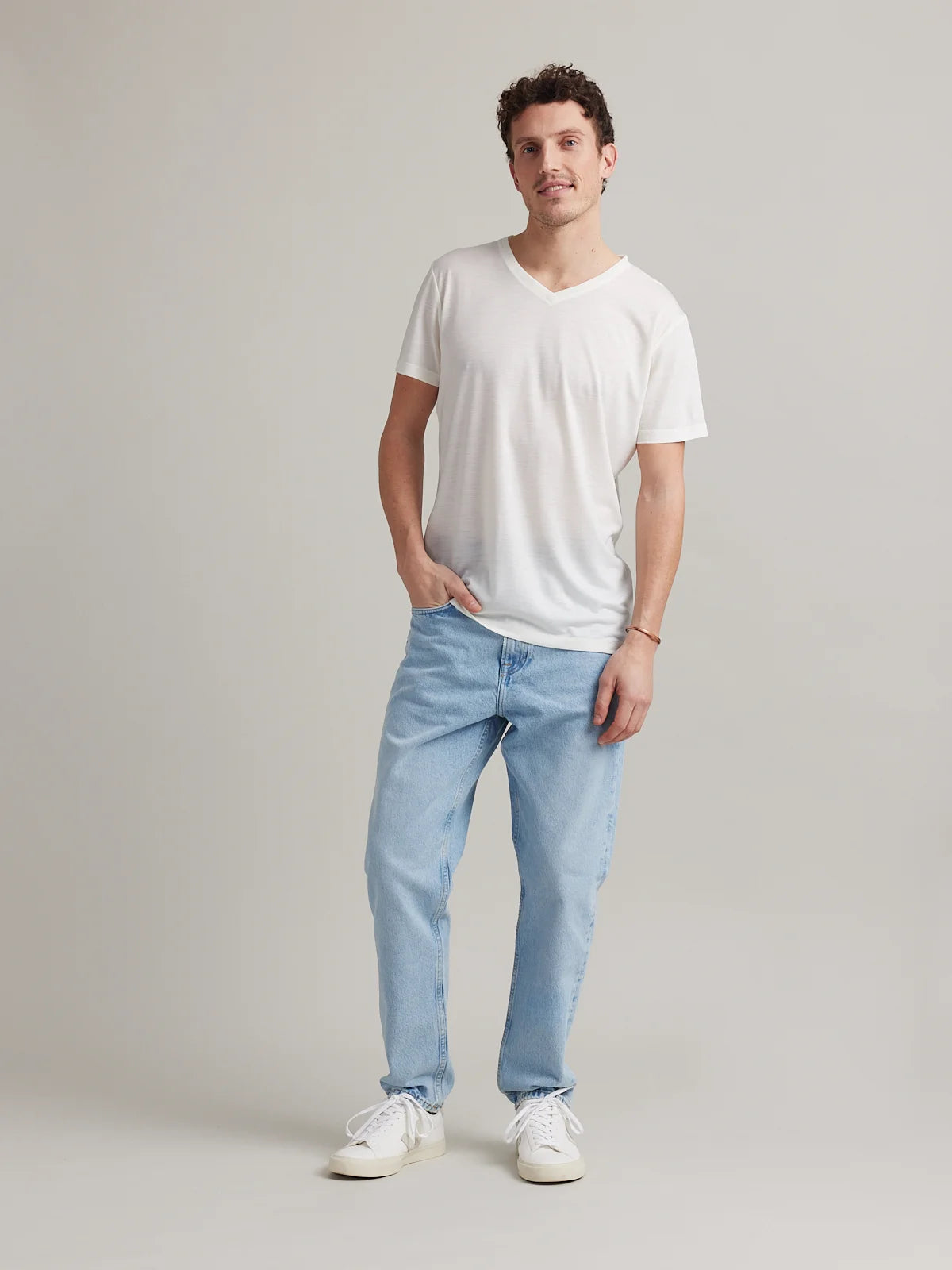 Male model wears a white merino wool T-shirt with V neck on a light blue denim jeans.