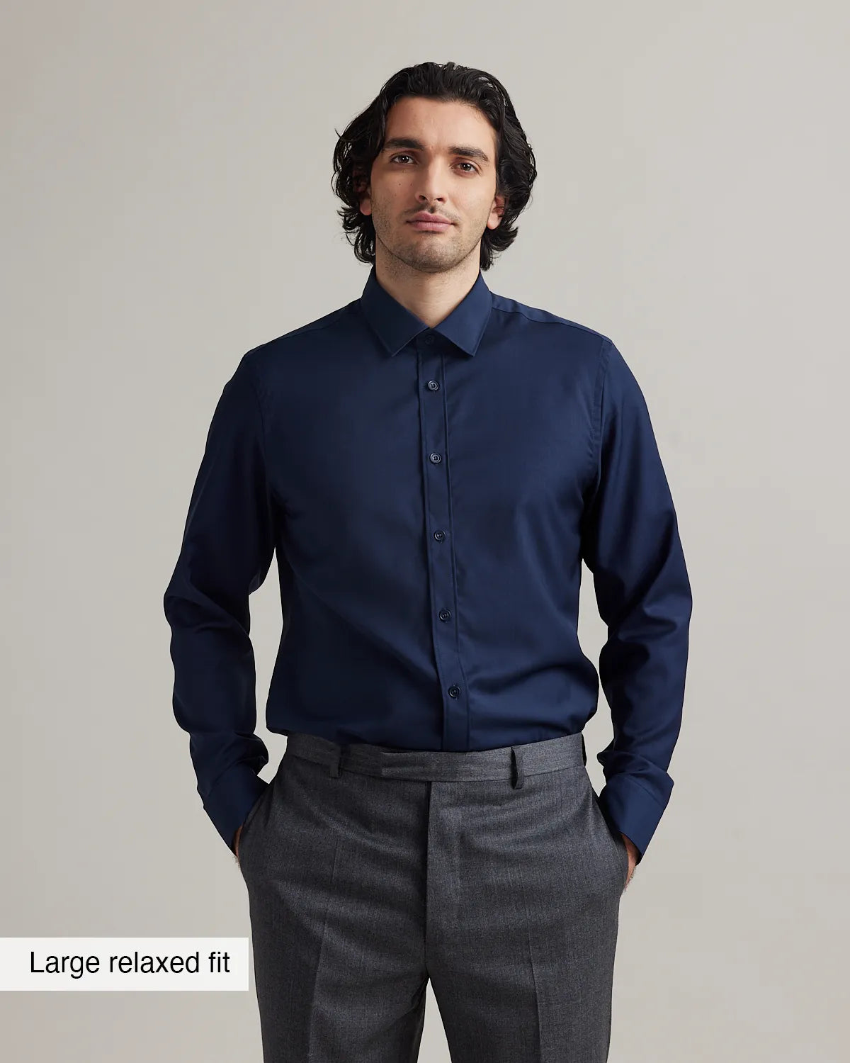 Man wearing a navy blue merinowool dress shirt in relaxed fit and gray pants on a plain background