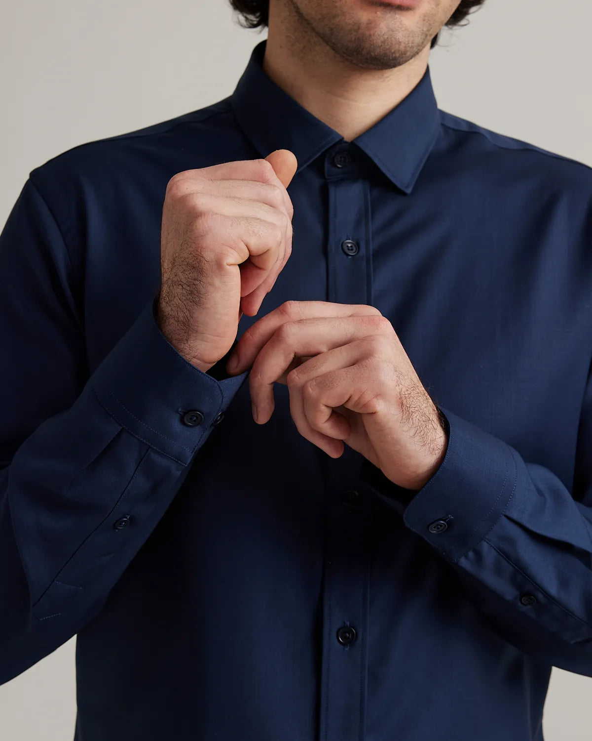 Man adjusting cuff on a navy blue merino shirt against a neutral background