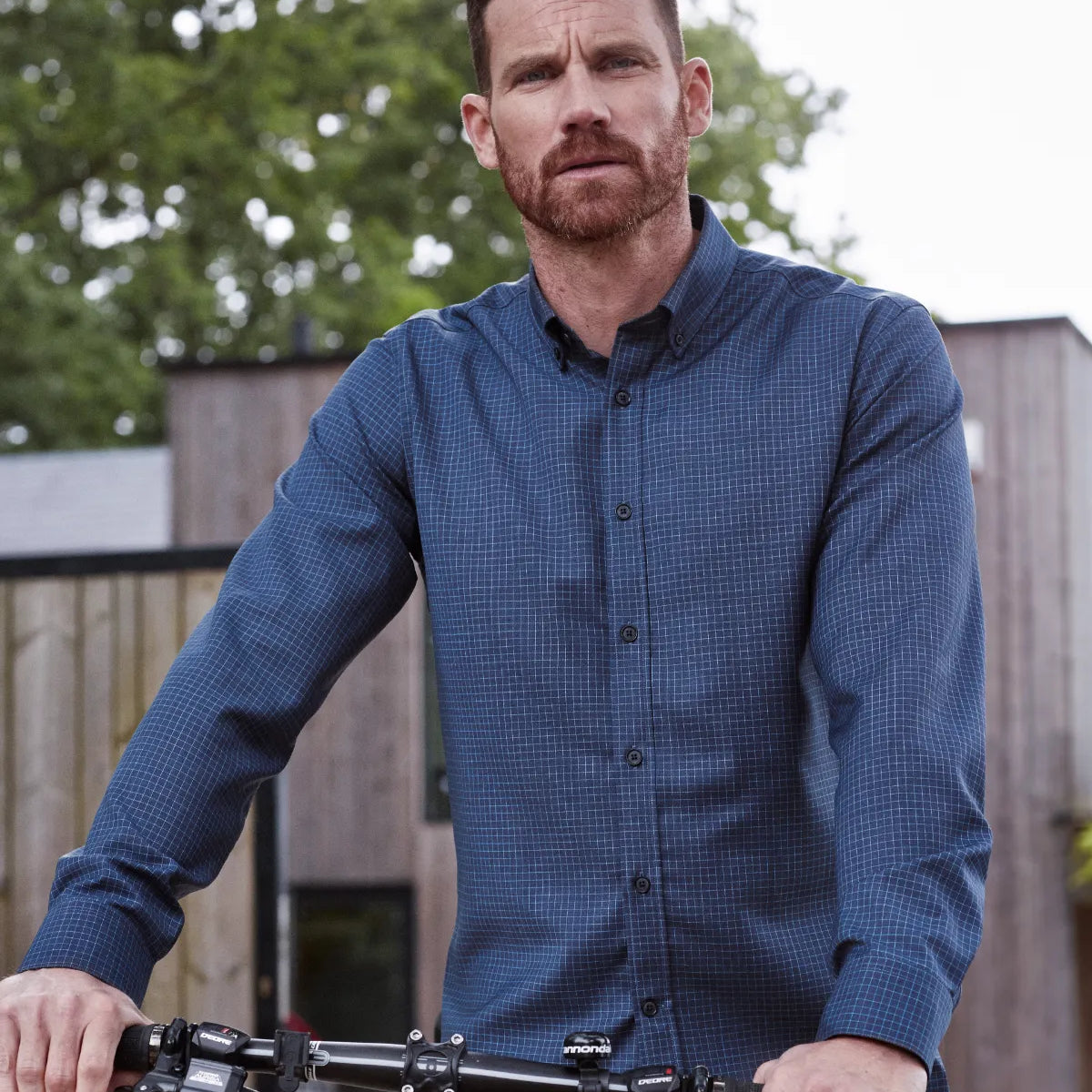 Man wearing a blue checkered merino shirt from Wolk standing next to a bicycle outdoors.