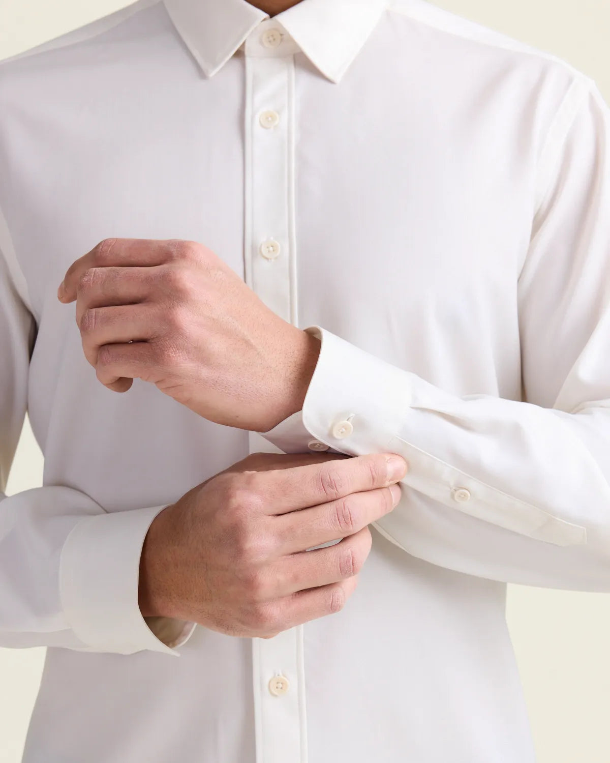 Person adjusting the cuff of a white merino wool dress shirt against a light background