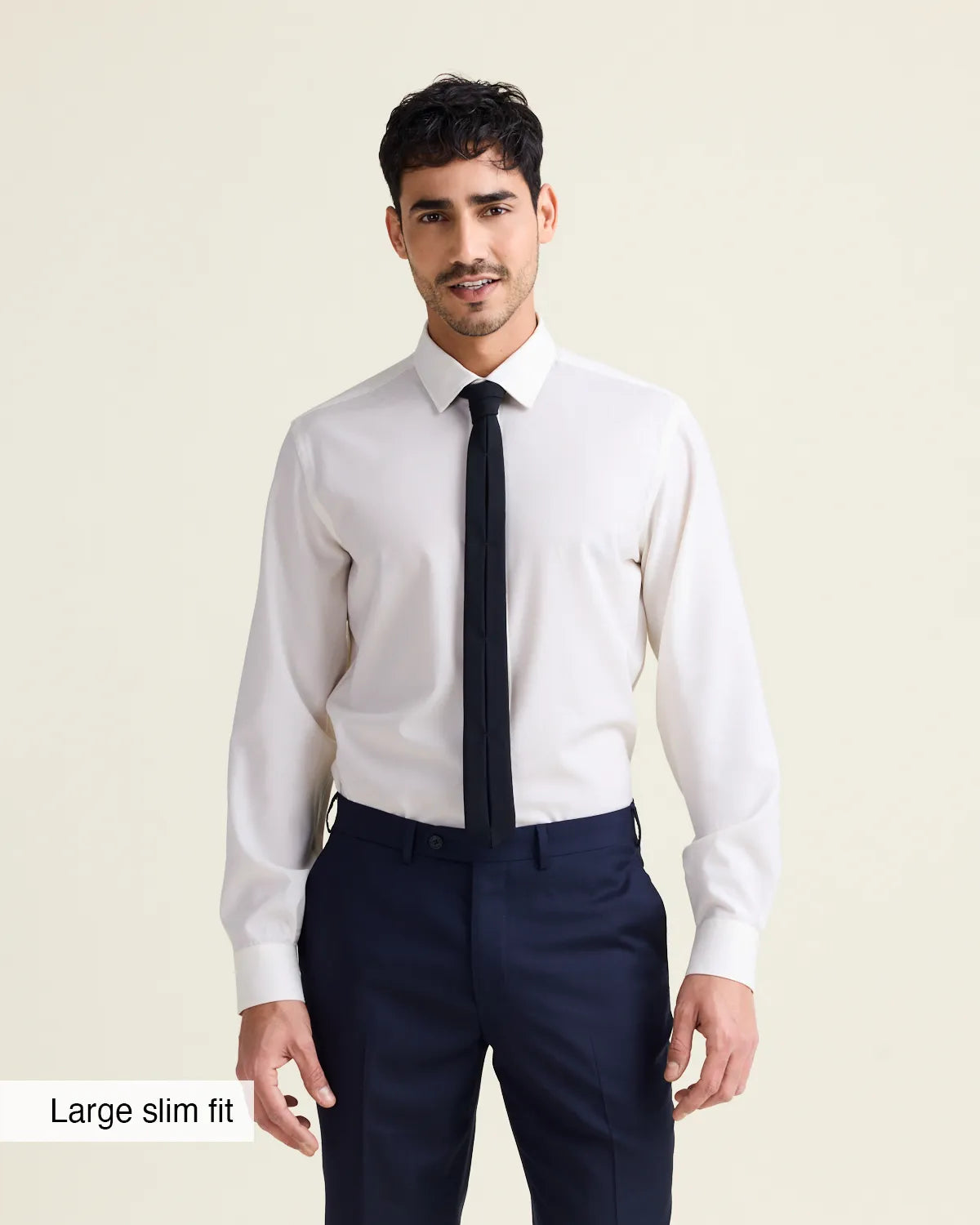 Man wearing a white merinowool dress shirt from in slim fit with navy trousers and a black tie on a beige background