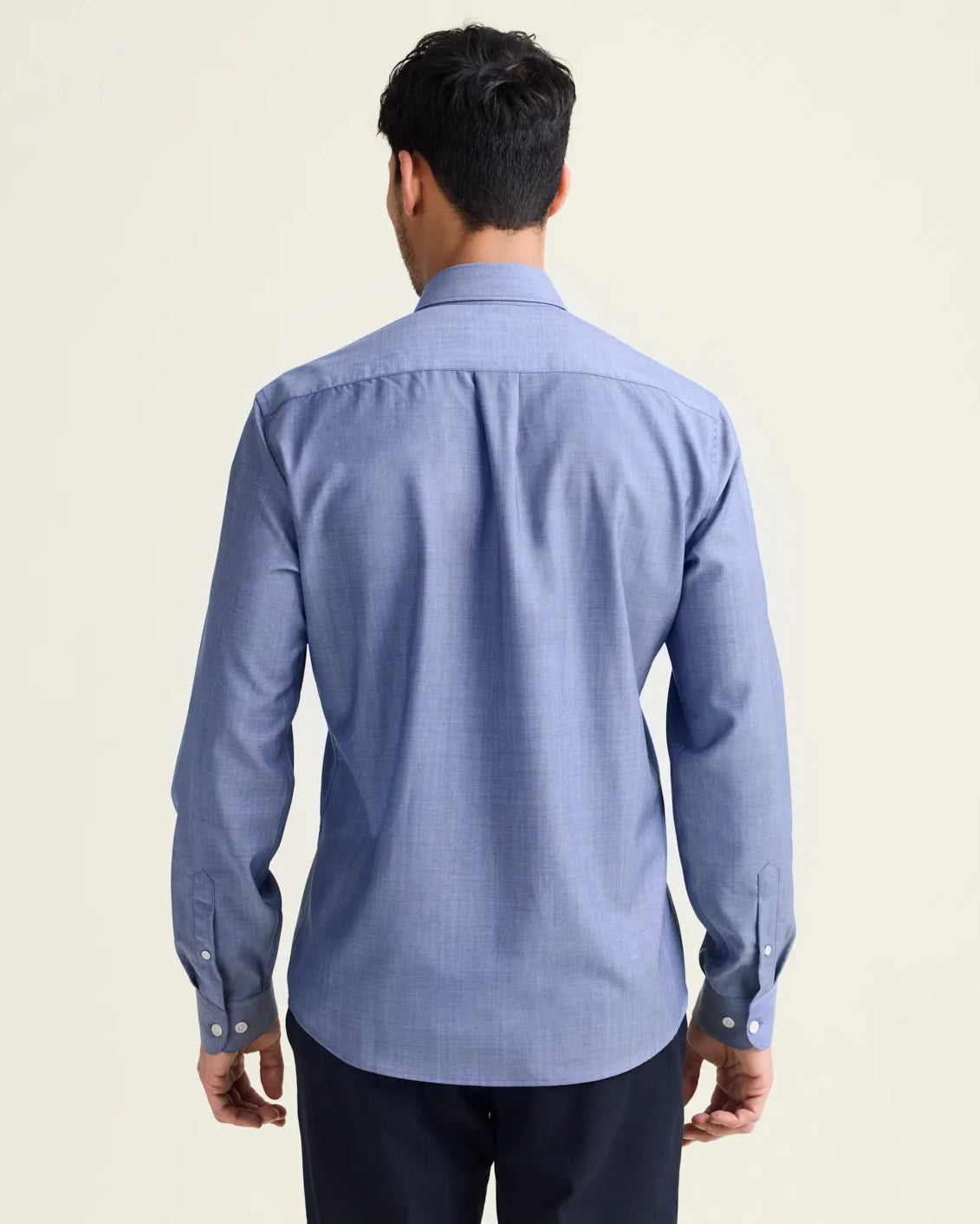 Backview of man wearing a light blue denim merino wool shirt from Wolk with long sleeves untucked on a navy pants