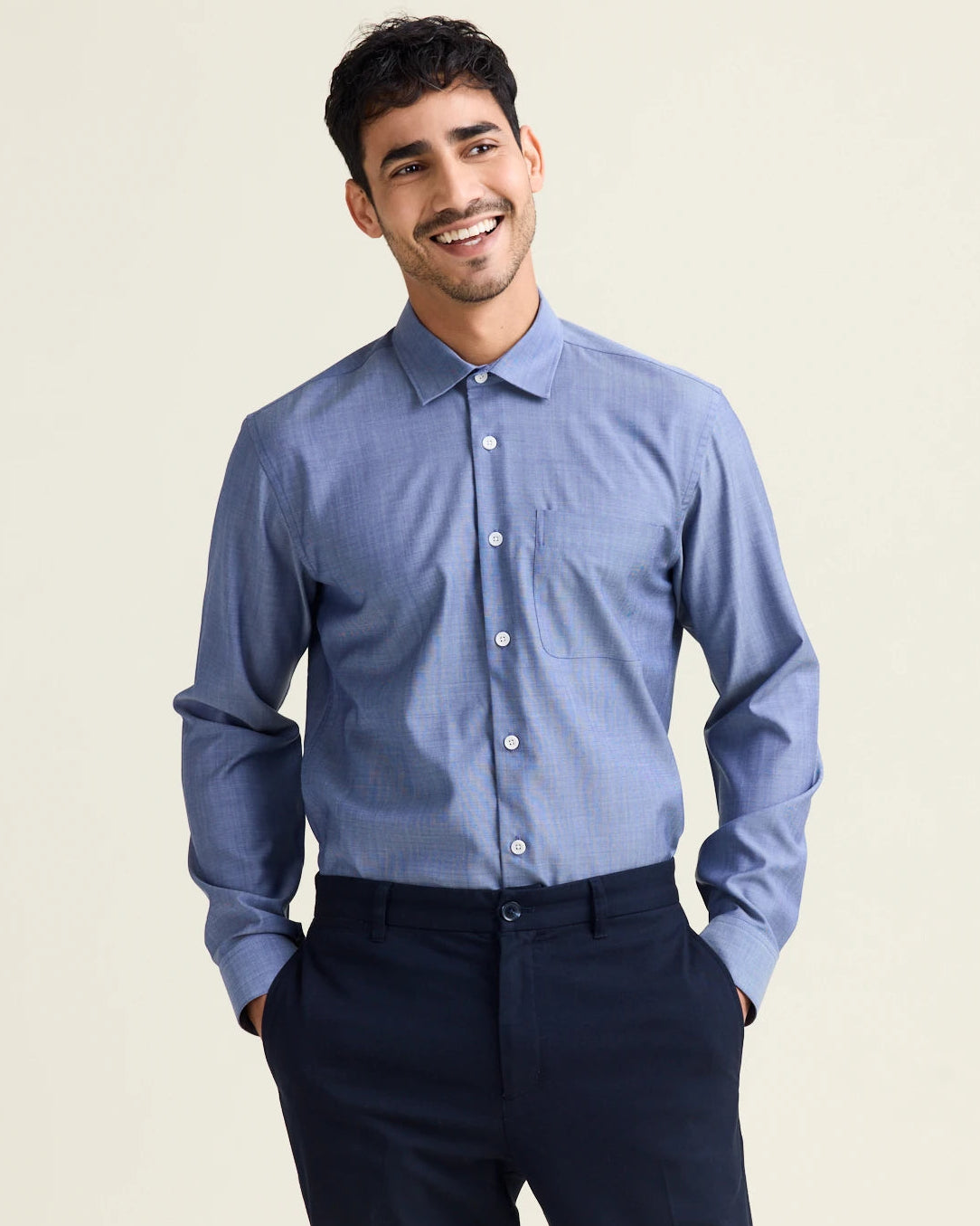 Man wearing a light blue merino dress shirt and dark pants against a beige background.
