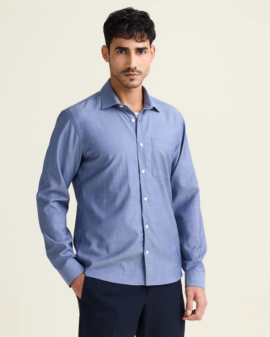 Man wears a merino wool shirt from Wolk in light blue denim color with chest pocket and white buttons untucked on a navy pants