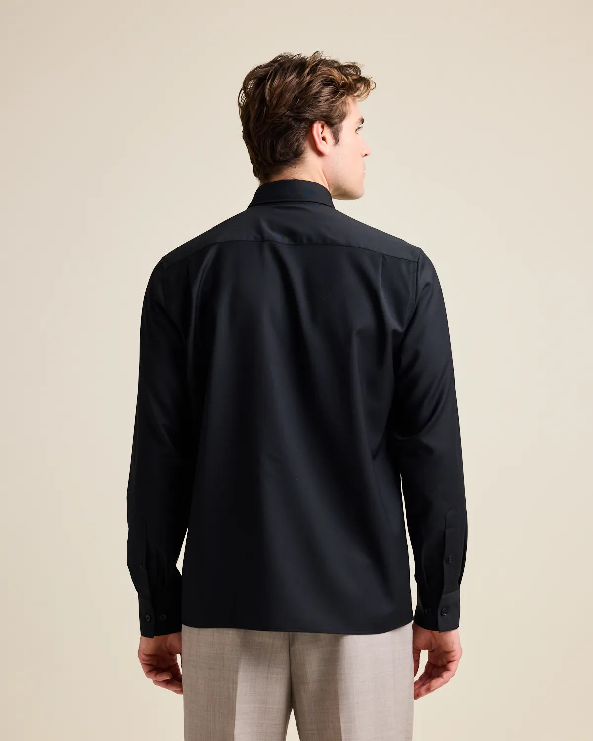 Back view of a man wearing a black merino wool shirt and beige pants against a beige background