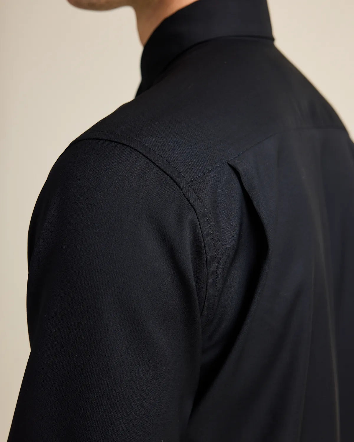 close up of the back pleat on a blck merino button up shirt
