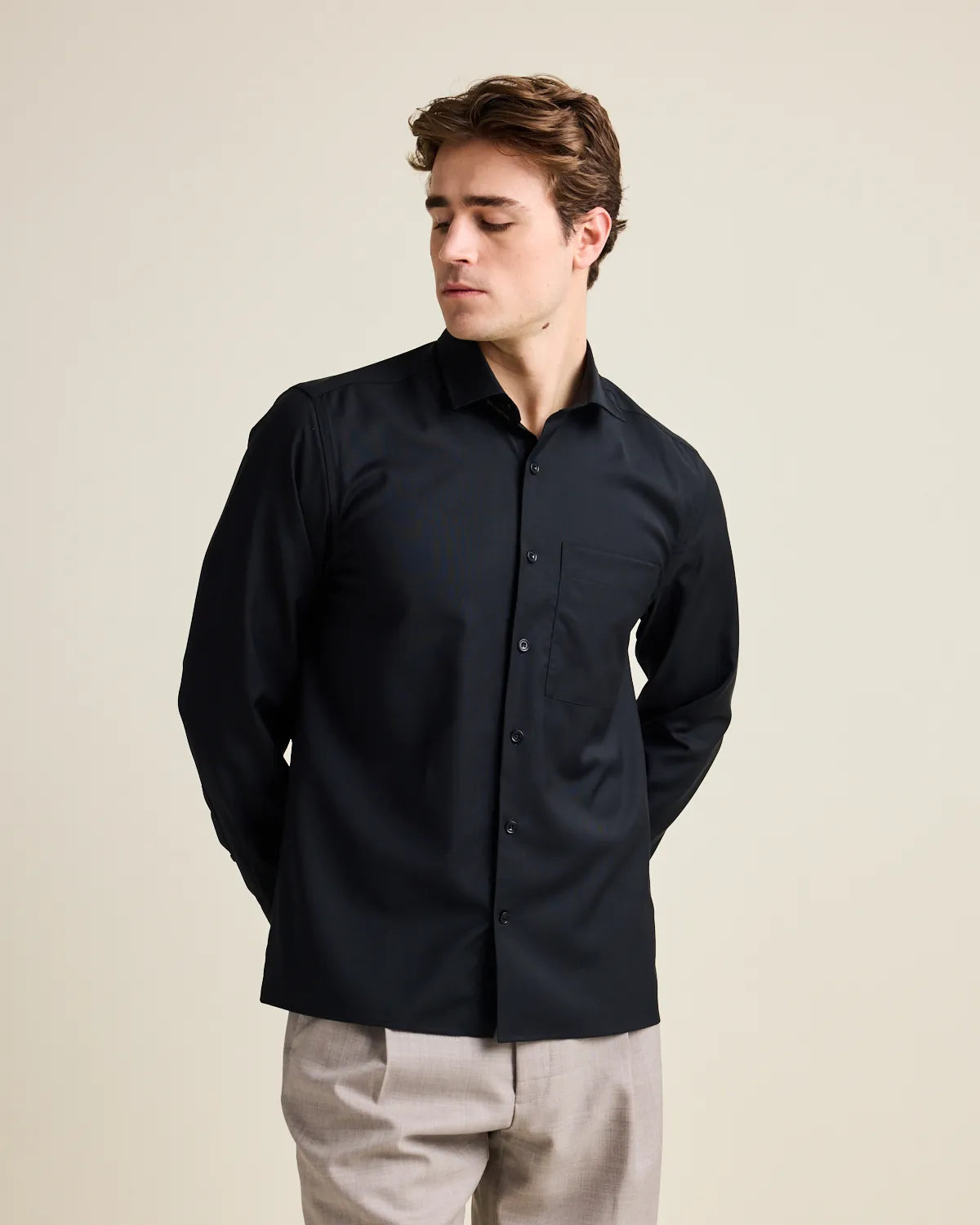 Man wearing a black merino button-up shirt against a beige background
