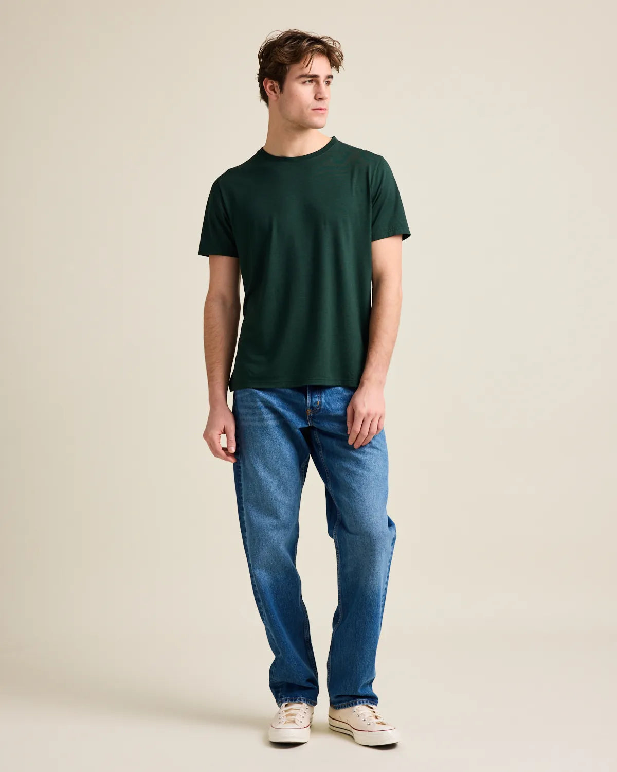 Man wearing a green t-shirt and blue jeans against a beige background