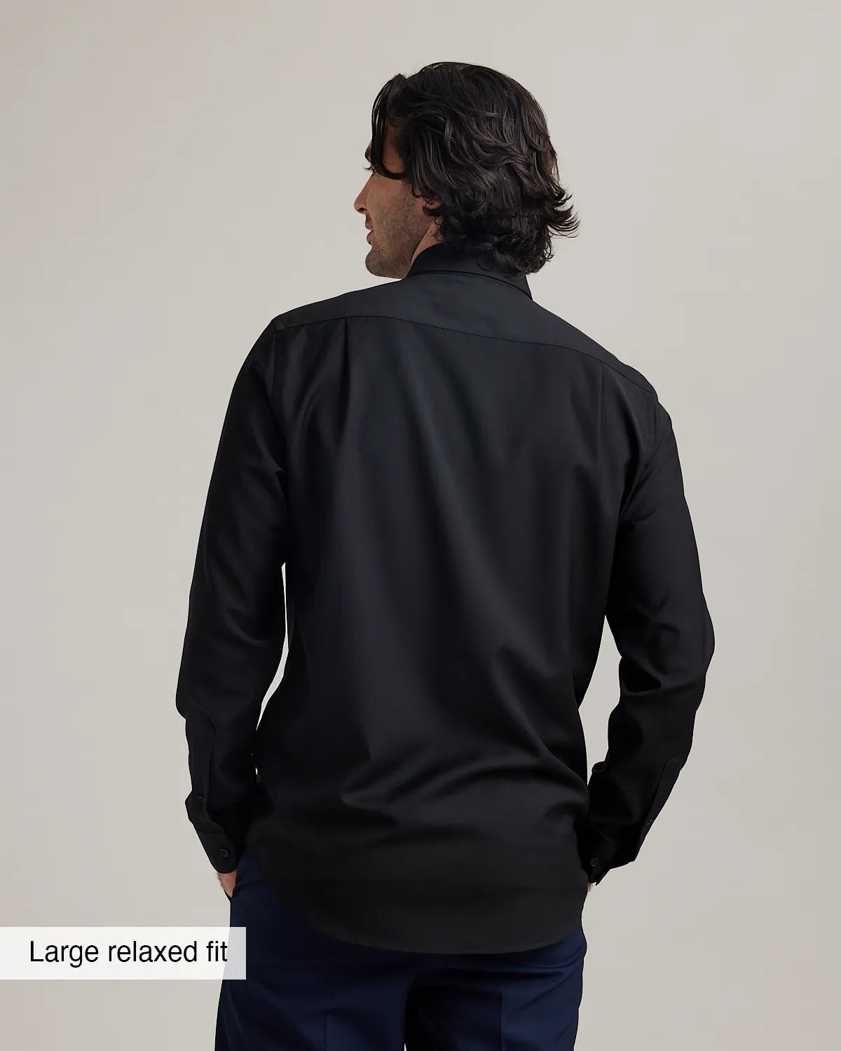 back view of a man wearing a black merinowool dress shirt with text 'Large relaxed fit' on a plain background