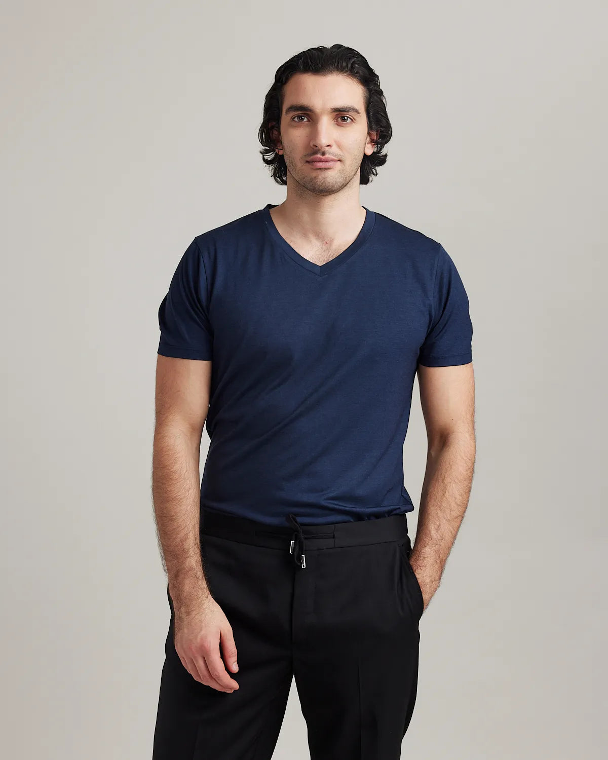 Man wearing a navy blue merino wool V-neck t-shirt and black pants on a plain background